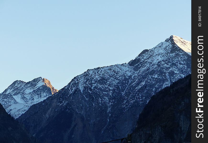 Peaks of snow capped mountain range with blue sky background.