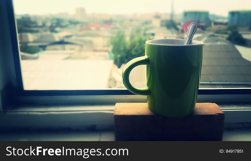 Cup of coffee on house window sill with city buildings in background.