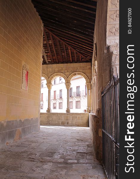 Stone corridor outside building with arched windows on sunny day.