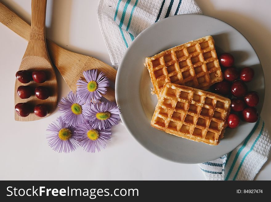 Overhead view of plate of cooked waffles on table with fresh cherries and flowers. Overhead view of plate of cooked waffles on table with fresh cherries and flowers.