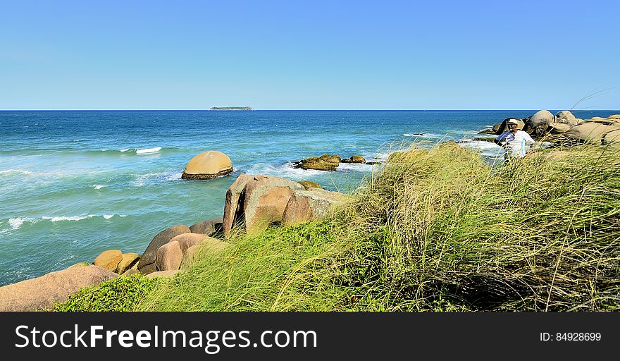 Person standing on rocky coastline on sunny day.