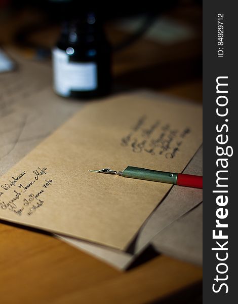 Old fashioned (retro) pen with steel nib and ink bottle lying next to a half finished letter or message on brown notepaper. Old fashioned (retro) pen with steel nib and ink bottle lying next to a half finished letter or message on brown notepaper.