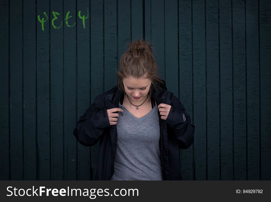 Smart young woman looking down while adjusting the black jacket over her gray knitted dress, dark painted wooden background. Smart young woman looking down while adjusting the black jacket over her gray knitted dress, dark painted wooden background.