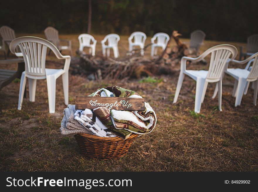 A fire pit with plastic chairs around it and a basket of blankets. A fire pit with plastic chairs around it and a basket of blankets.