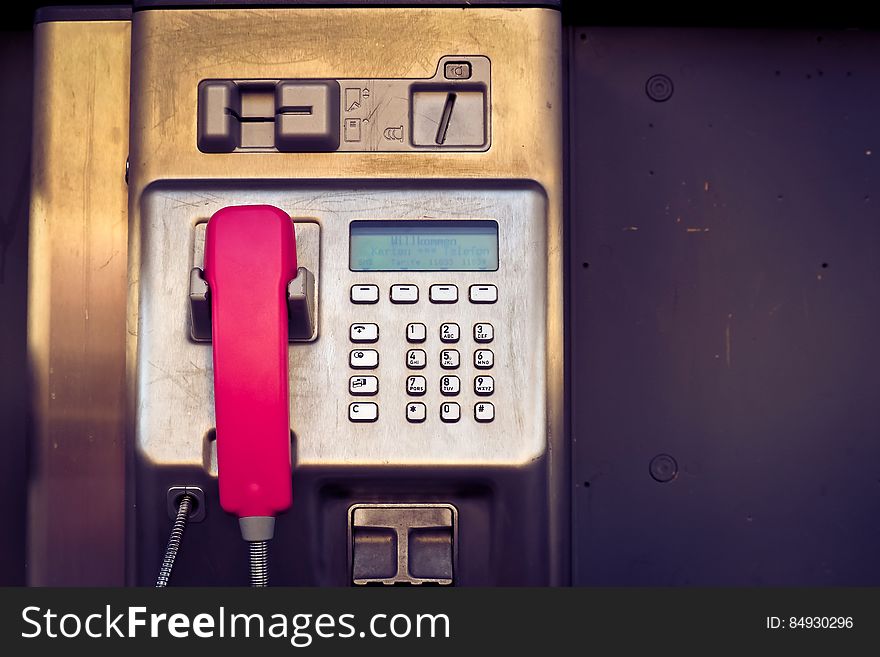 Closeup of a public pay phone with a red handset and silver button keypad. Closeup of a public pay phone with a red handset and silver button keypad.