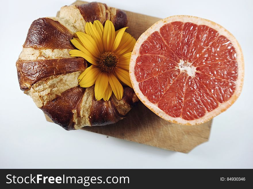 A croissant and a half of red grapefruit decorated with a yellow flower. A croissant and a half of red grapefruit decorated with a yellow flower.