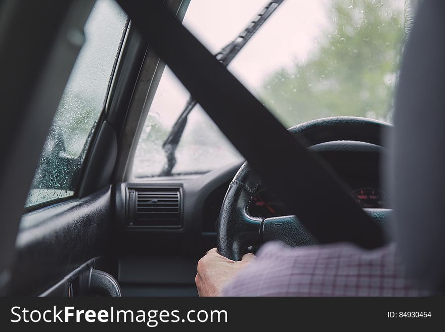 Car interior, fastened seat belt, a hand holding steering wheel.