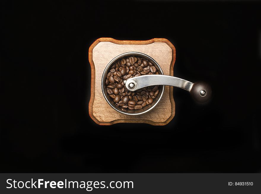 Antique (or retro) coffee grinder with coffee beans in the tub and curved handle viewed directly from above, black background.