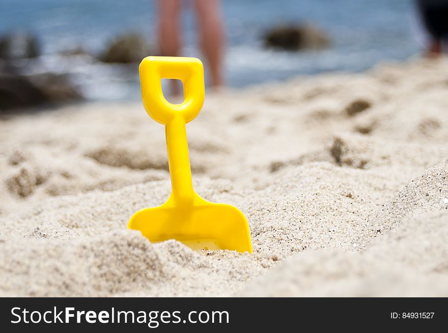 Closeup of a yellow plastic spade on the beach symbol of Summer holidays at the seaside background of sea and sky.