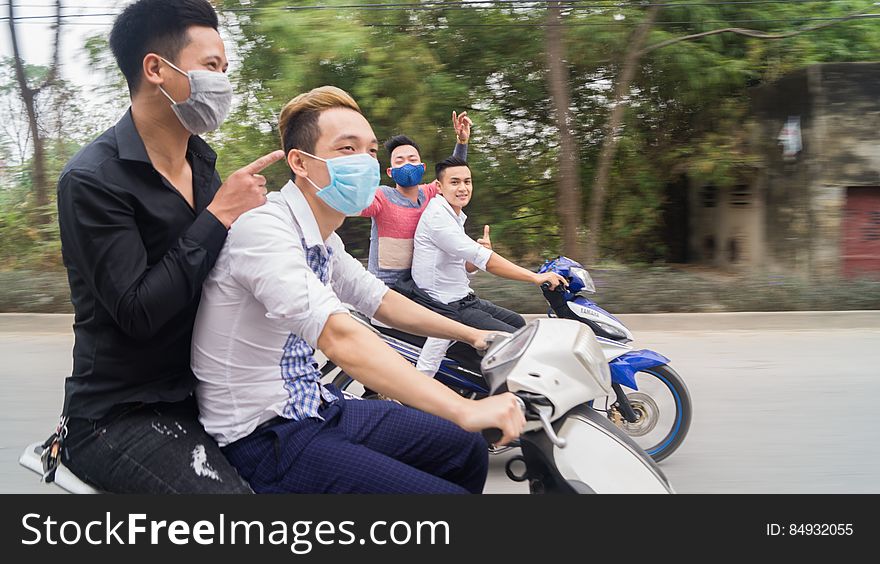 Asian men wearing face masks riding motor scooters on street. Asian men wearing face masks riding motor scooters on street.