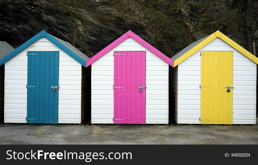 Colorful bathing huts in white but with blue, pink (mauve) and yellow doors situated at the bottom of a cliff. Colorful bathing huts in white but with blue, pink (mauve) and yellow doors situated at the bottom of a cliff.