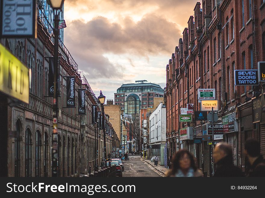 Person On Road Between Brown Walled Building During Daytime Under Cumulus Clouds