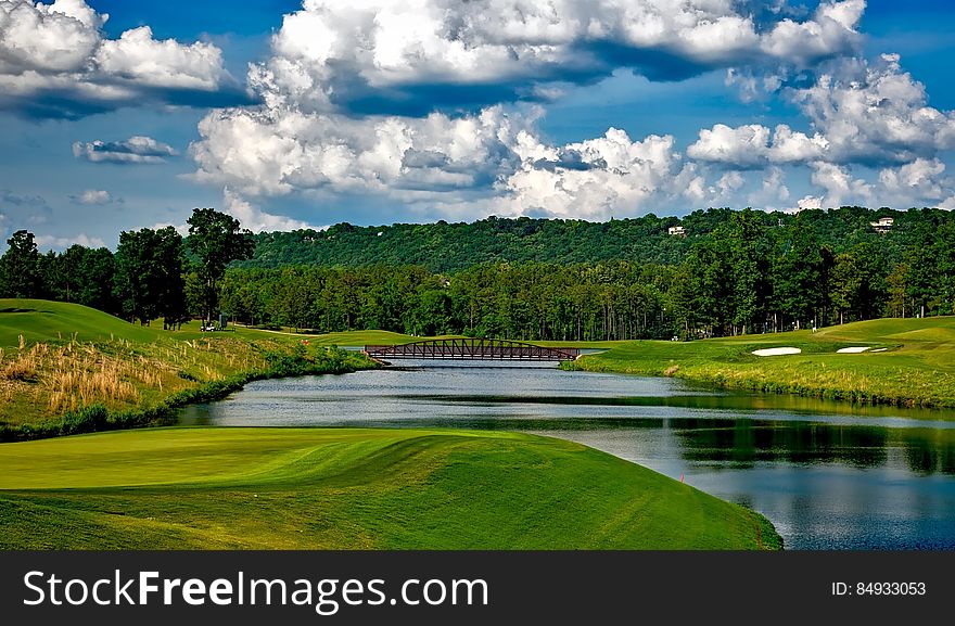 A river running through a green, rolling golf course with fluffy, white clouds in a blue sky. A river running through a green, rolling golf course with fluffy, white clouds in a blue sky.