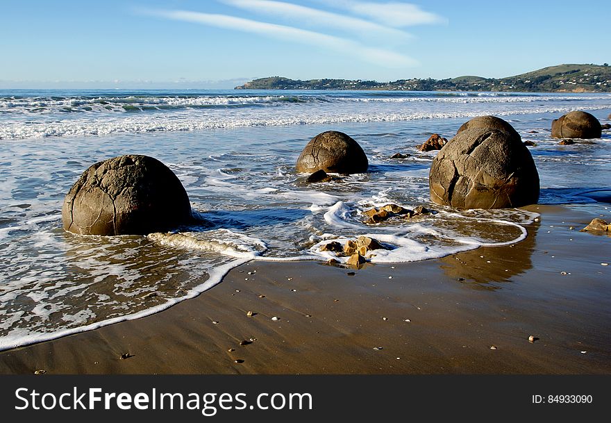The Moeraki Boulders are unusually large and spherical boulders lying along a stretch of Koekohe Beach on the wave cut Otago coast of New Zealand between Moeraki and Hampden. They occur scattered either as isolated or clusters of boulders within a stretch of beach where they have been protected in a scientific reserve. The erosion by wave action of mudstone, comprising local bedrock and landslides, frequently exposes embedded isolated boulders. These boulders are grey-colored septarian concretions, which have been exhumed from the mudstone enclosing them and concentrated on the beach by coastal erosion. The Moeraki Boulders are unusually large and spherical boulders lying along a stretch of Koekohe Beach on the wave cut Otago coast of New Zealand between Moeraki and Hampden. They occur scattered either as isolated or clusters of boulders within a stretch of beach where they have been protected in a scientific reserve. The erosion by wave action of mudstone, comprising local bedrock and landslides, frequently exposes embedded isolated boulders. These boulders are grey-colored septarian concretions, which have been exhumed from the mudstone enclosing them and concentrated on the beach by coastal erosion