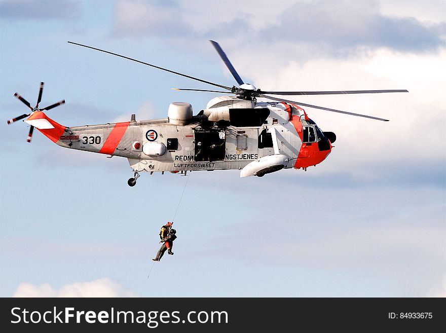 An ongoing air sea rescue operation with a Sea King helicopter and operator lifting a person with a cable.