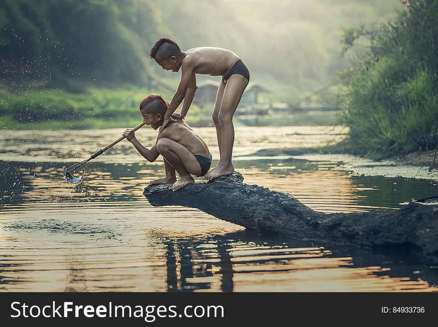 A pair of young Asian boys spear fishing on a river. A pair of young Asian boys spear fishing on a river.