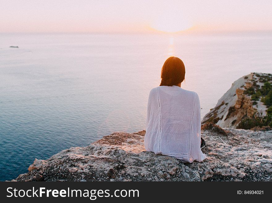 A woman sitting on a rock at the seaside watching the sun near the horizon. A woman sitting on a rock at the seaside watching the sun near the horizon.