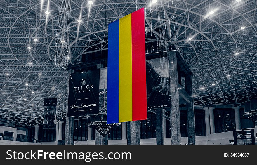 The Romanian flag hanging from a ceiling in a conference center or mall.