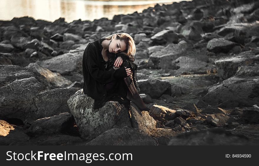 A woman sitting on the rocks of a rocky shore. A woman sitting on the rocks of a rocky shore.