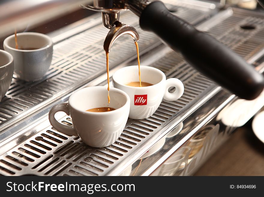 Two cups below an espresso machine being filled with espresso. Two cups below an espresso machine being filled with espresso.