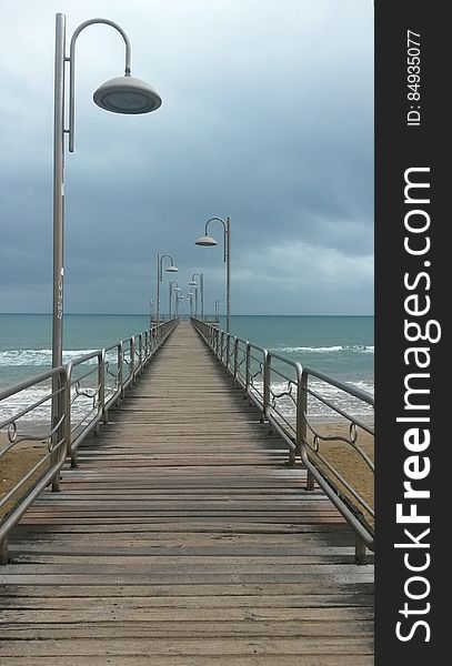 A boardwalk with lamps and metal railing across a sandy beach, open sea in the background. A boardwalk with lamps and metal railing across a sandy beach, open sea in the background.