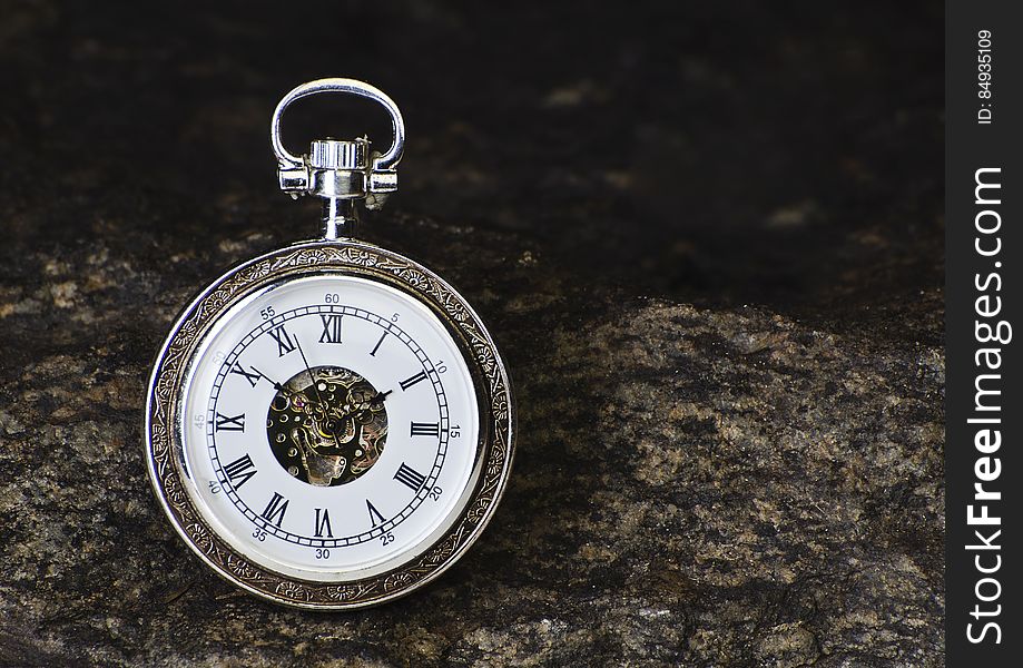 A close up of an ornamental analog watch on a rocky background.