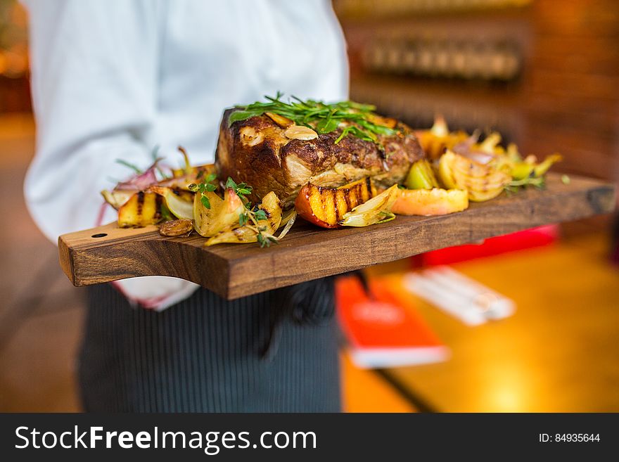 A chef serving a wood tray with roasted meat.