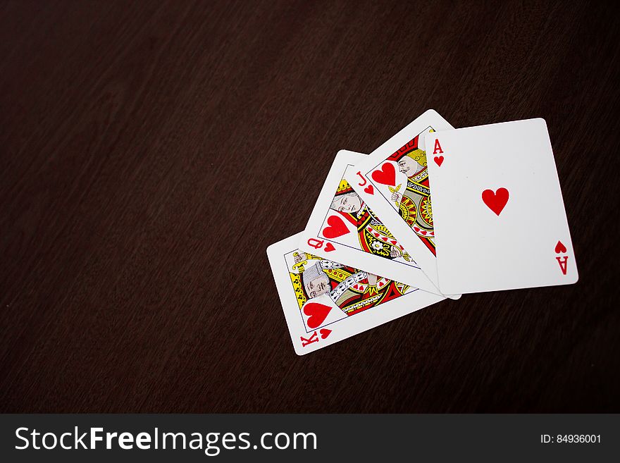 Playing cards with Ace, Jack, Queen and King of Hearts fanned out on a dark background.