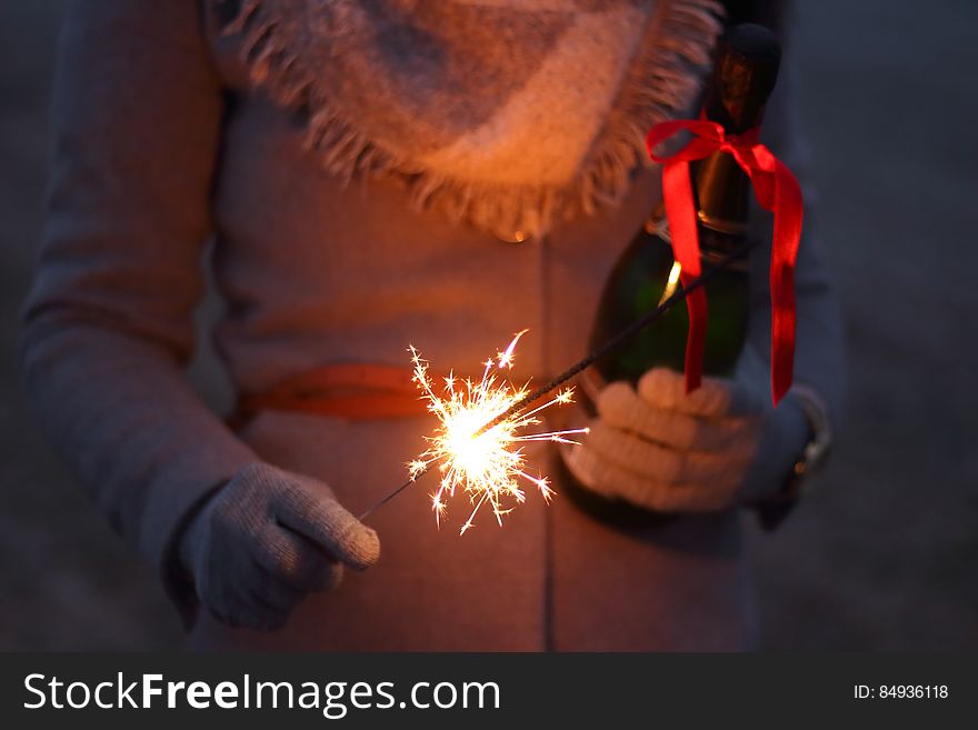 A close up of a person in winter clothes holding a bottle of champagne and a sparkler. A close up of a person in winter clothes holding a bottle of champagne and a sparkler.