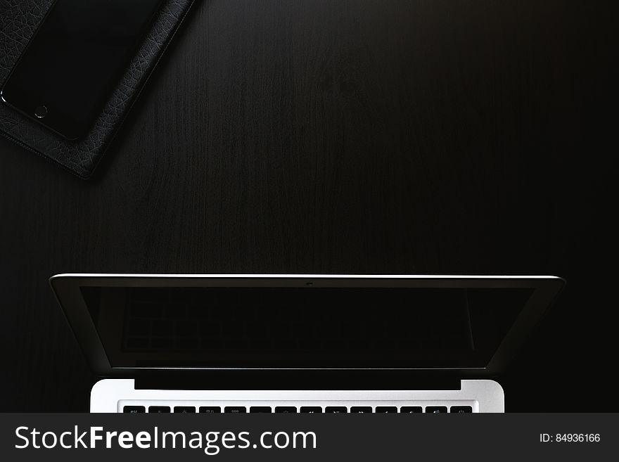 The monitor of a switched off laptop and a smartphone next to it on a black table. The monitor of a switched off laptop and a smartphone next to it on a black table.