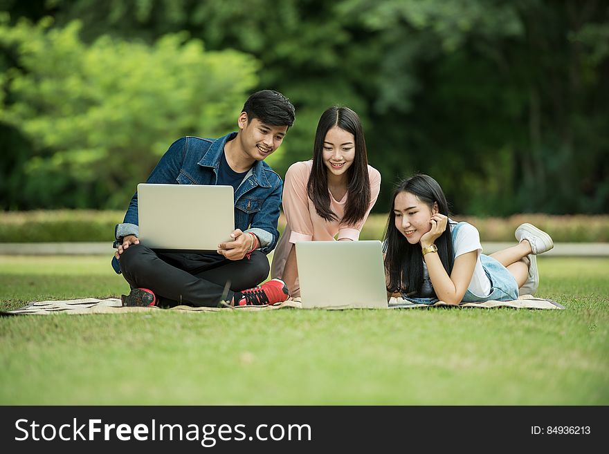 Three smiling teenagers on the grass looking at their laptops. Three smiling teenagers on the grass looking at their laptops.
