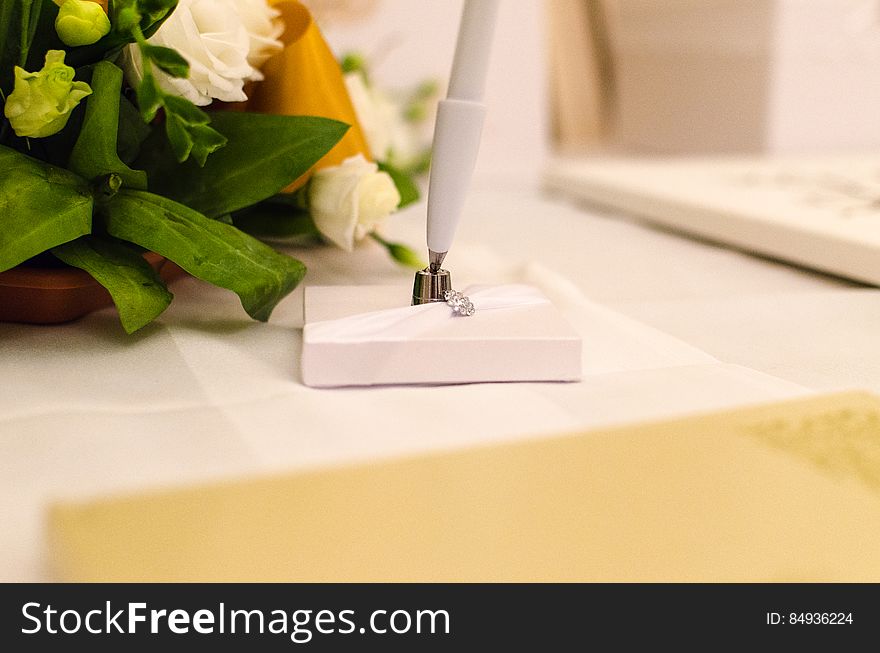 A flower arrangement with white roses and an elegant white pen next to it. A flower arrangement with white roses and an elegant white pen next to it.