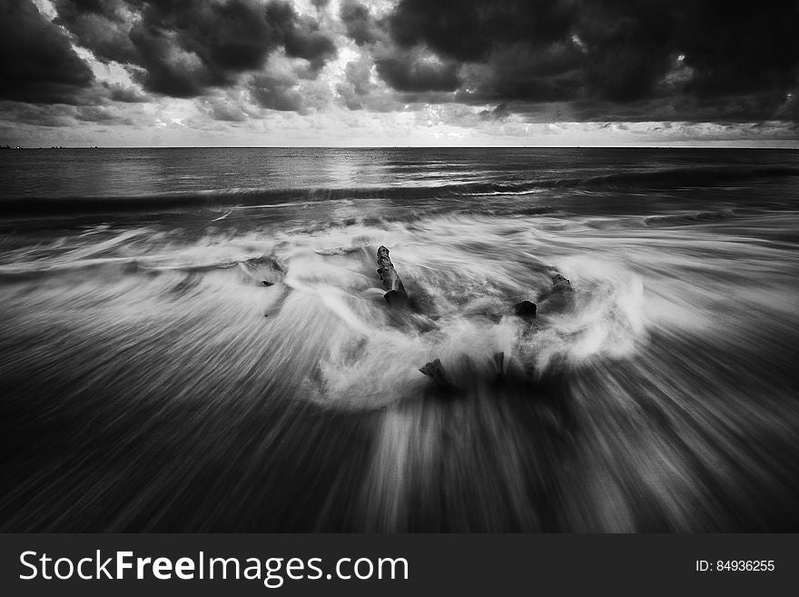 A monochrome photo of splashy waves on a beach and dark clouds above. A monochrome photo of splashy waves on a beach and dark clouds above.