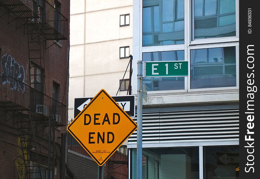 A yellow dead end street sign and buildings in the background. A yellow dead end street sign and buildings in the background.