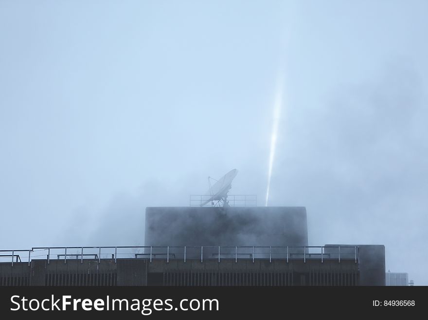 A satellite dish on the roof of a building in foggy weather. A satellite dish on the roof of a building in foggy weather.