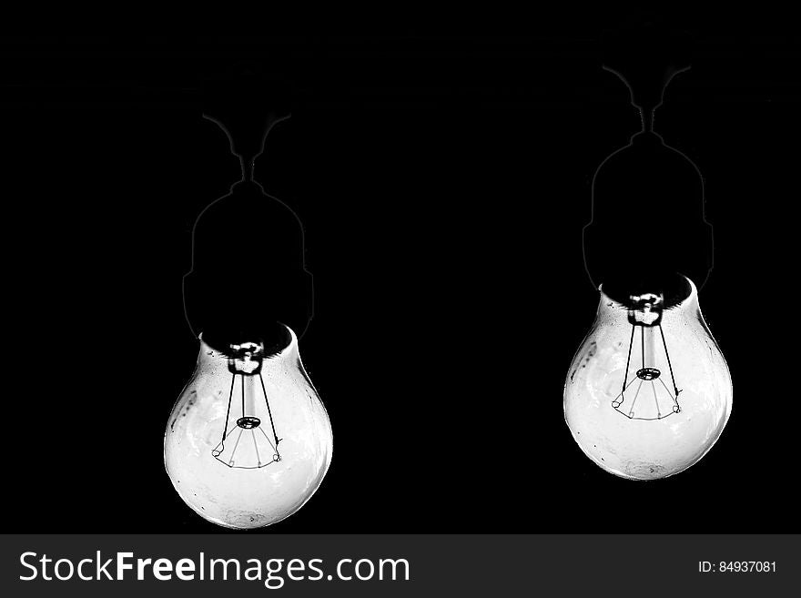 Closeup of two bright retro style filament bulbs with sockets and wires just visible on a black background. Closeup of two bright retro style filament bulbs with sockets and wires just visible on a black background.