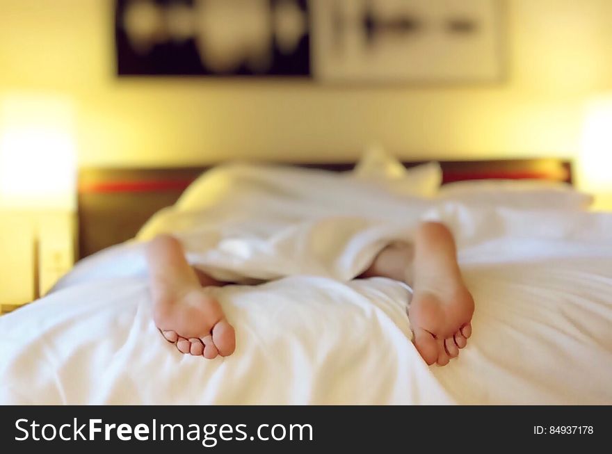 Woman in white dress lying prone on top of bedspread with selective focus on the soles of her feet, bedroom background. Woman in white dress lying prone on top of bedspread with selective focus on the soles of her feet, bedroom background.