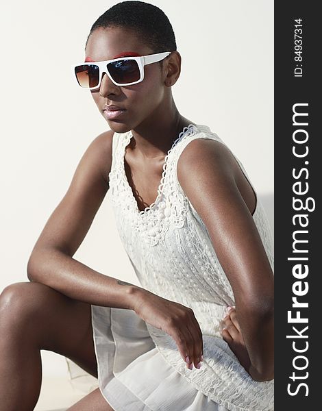 Woman Wearing White Tank Dress and White Frame Sunglasses Sitting and Making a Pose