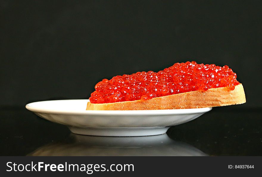 Side view of salmon eggs on slice of bread for breakfast, black background.