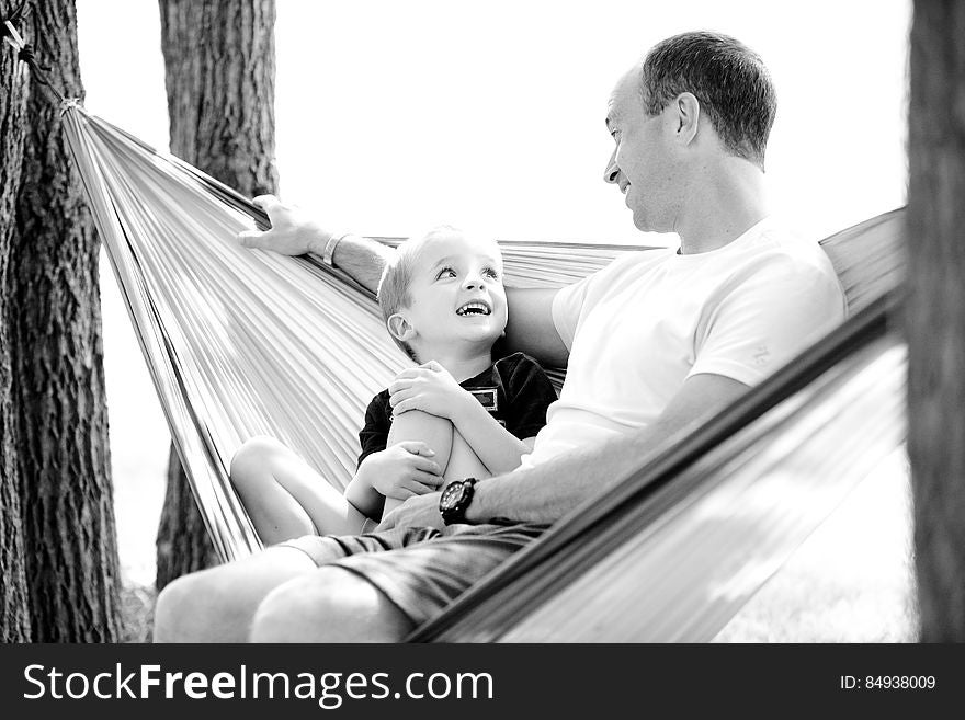 A black and white photo of a father and his son sitting in a hammock looking at each other and smiling. A black and white photo of a father and his son sitting in a hammock looking at each other and smiling.