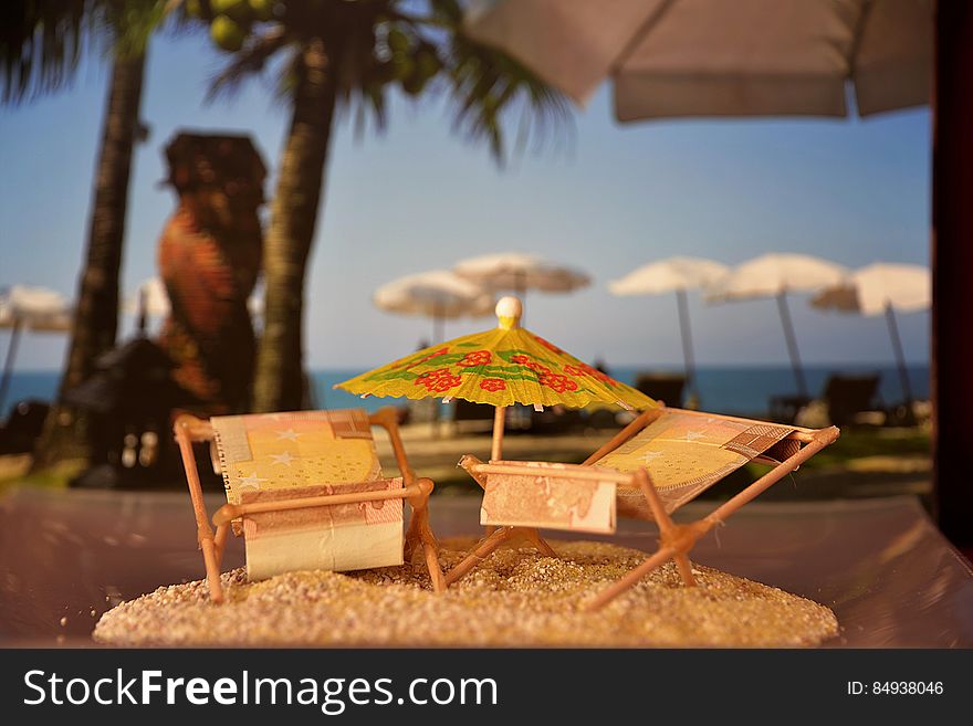 A close up of a miniature model of a parasole and two sunbeds on sand, tropical beach in the background. A close up of a miniature model of a parasole and two sunbeds on sand, tropical beach in the background.