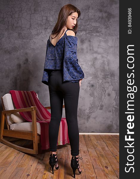 Attractive young Asian girl (Japanese) posing while wearing blue top, black tight fitting trousers and extremely high heels. Bare room except for one easy chair and gray wall. Attractive young Asian girl (Japanese) posing while wearing blue top, black tight fitting trousers and extremely high heels. Bare room except for one easy chair and gray wall.