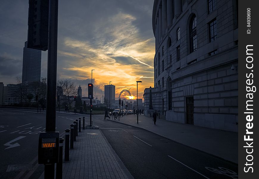 London street at sunset with historic stone building on the right and London Eye in the distance highlighted by a golden sky.