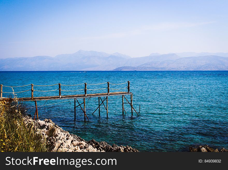 A small wooden pier on in the water with mountains on the distance.