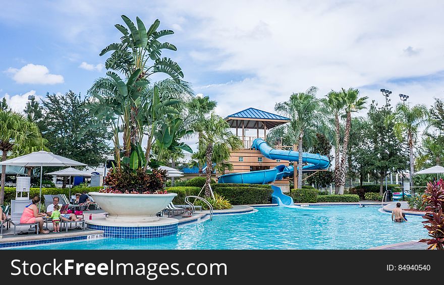 A view from a tropical resort with swimming pool, slide and sun chairs.