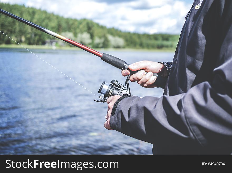 A person fishing with an open reel fishing pole.