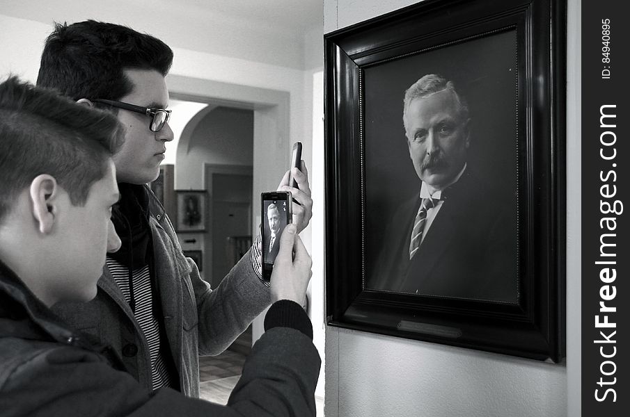 A pair of men taking a photo of a painting with smartphone. A pair of men taking a photo of a painting with smartphone.