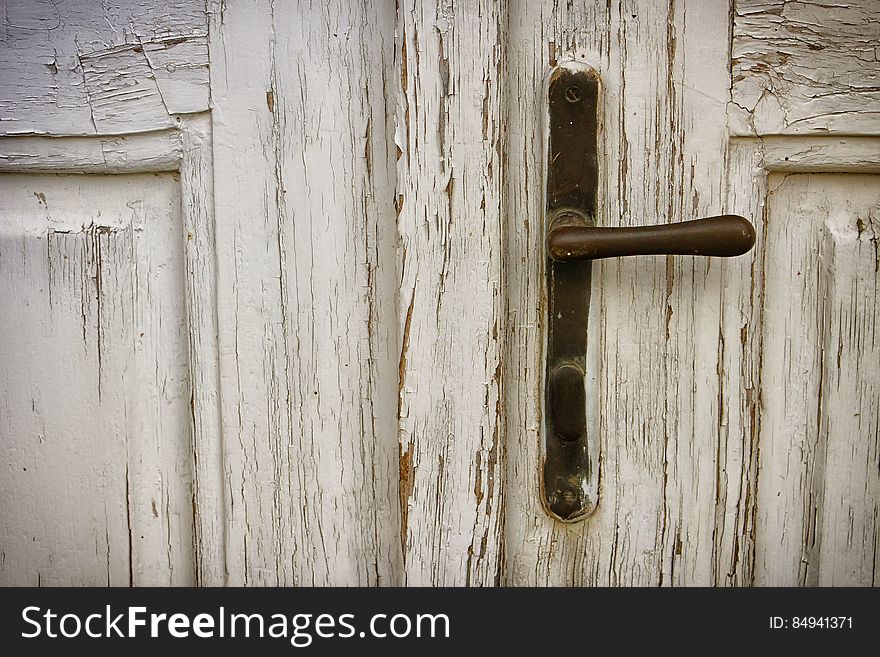 Closeup of a brown door handle on a peeling white rustic door. Closeup of a brown door handle on a peeling white rustic door.