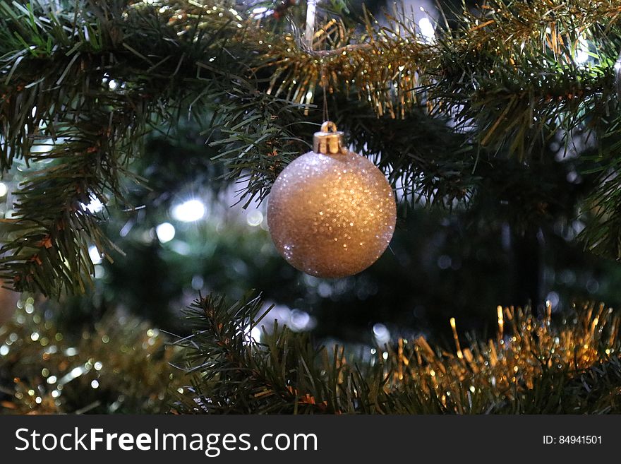 Closeup of a round sparkling gold Christmas ornament, hanging on a tree decorated with gold garland. Closeup of a round sparkling gold Christmas ornament, hanging on a tree decorated with gold garland.