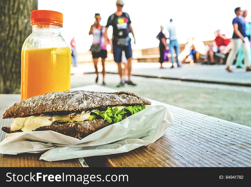 A sandwich and orange juice on a table outdoors. A sandwich and orange juice on a table outdoors.